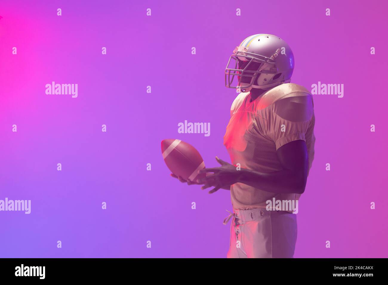 African american male american football player holding ball with neon pink and purple lighting. Sport, movement, training and active lifestyle concept Stock Photo