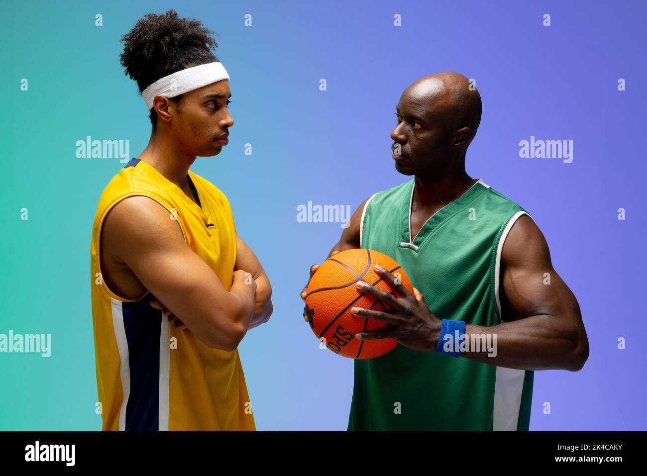 Image of two diverse basketball players facing each other on purple to green background. Sports and competition concept. Stock Photo