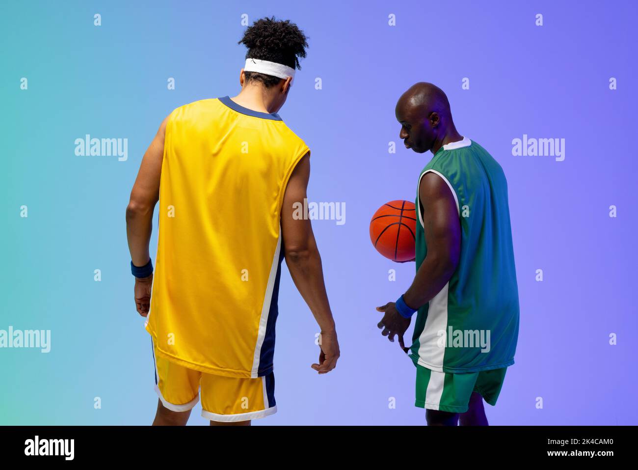 Image of two diverse basketball players with basketball on purple to green background. Sports and competition concept. Stock Photo