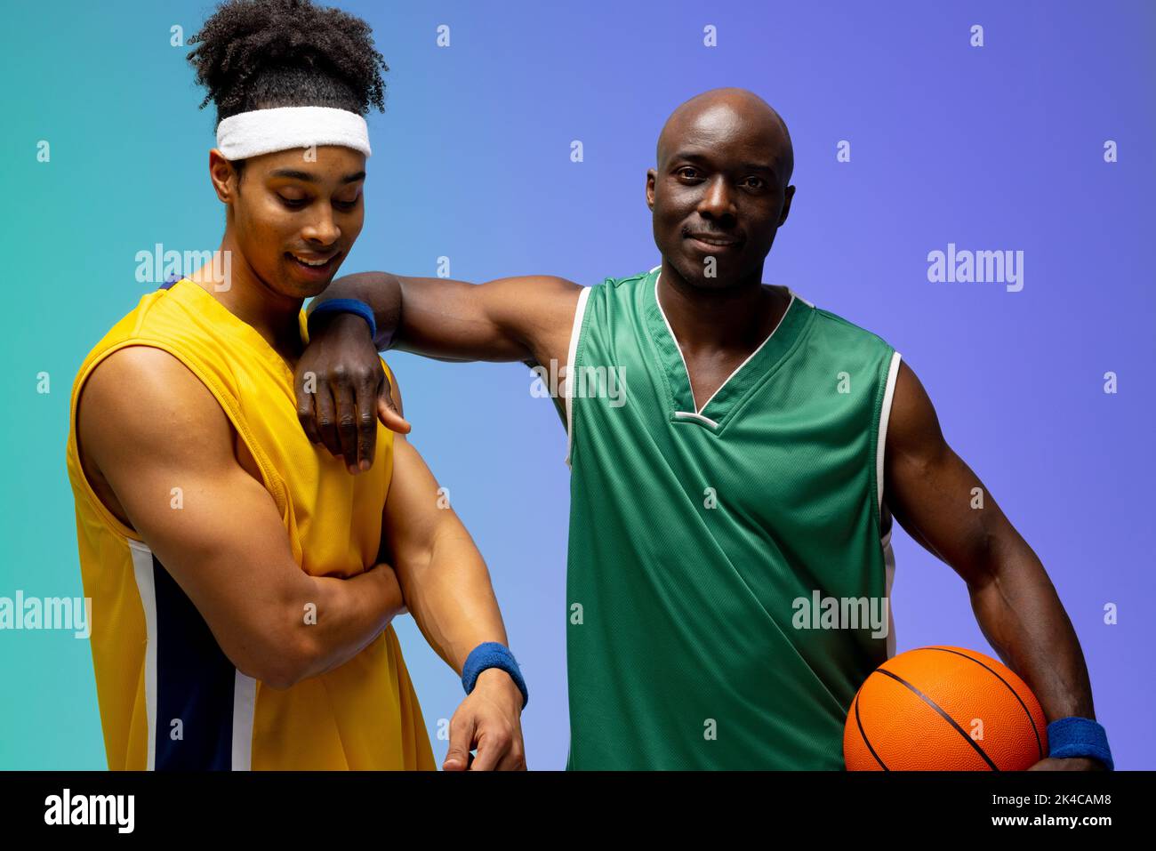 Image of portrait of two diverse basketball players with basketball on purple to green background. Sports and competition concept. Stock Photo