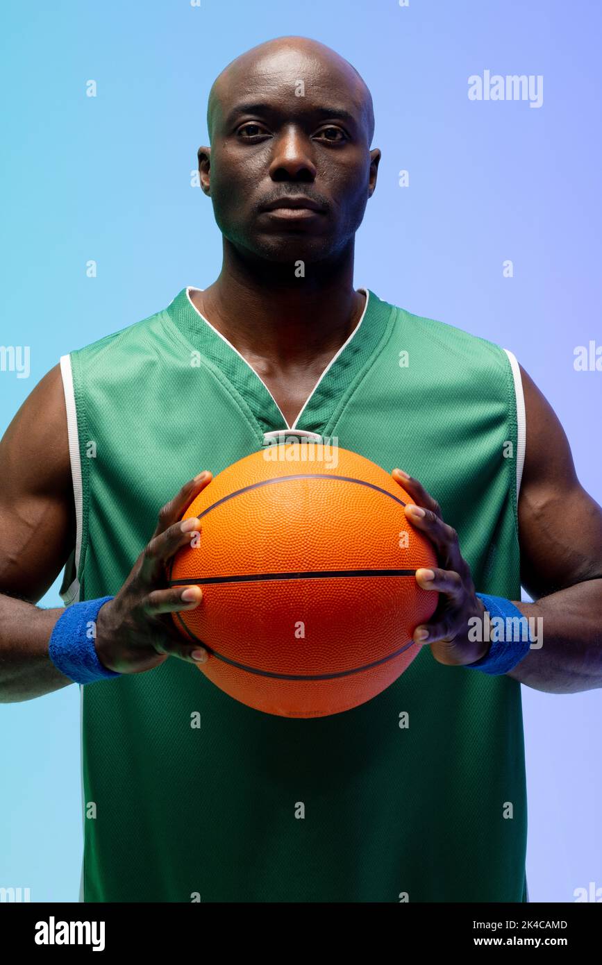 Image of portrait of african american basketball player with basketball on green to blue background. Sports and competition concept. Stock Photo