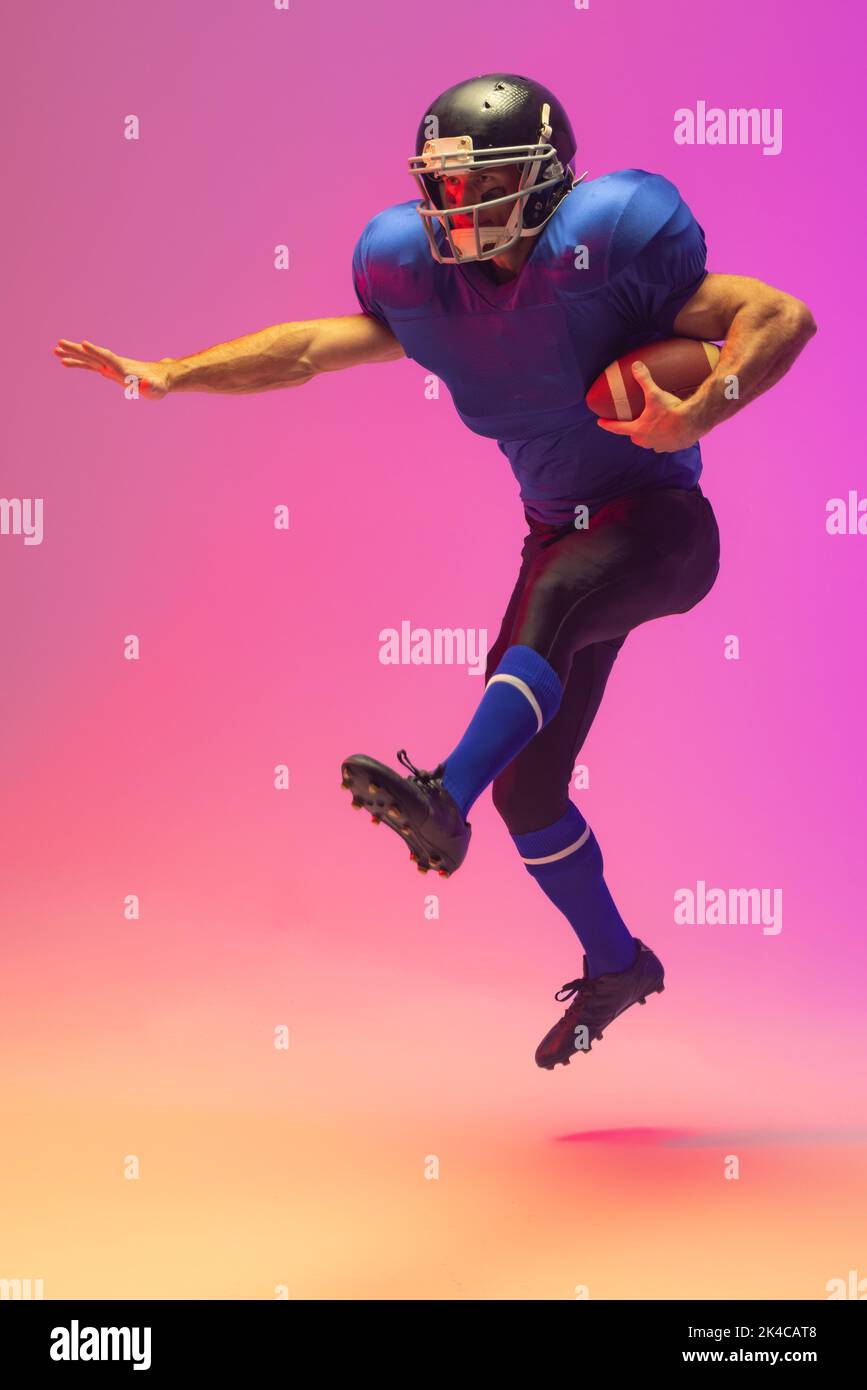 Caucasian male american football player holding ball with neon pink lighting. Sport, movement, training and active lifestyle concept. Stock Photo
