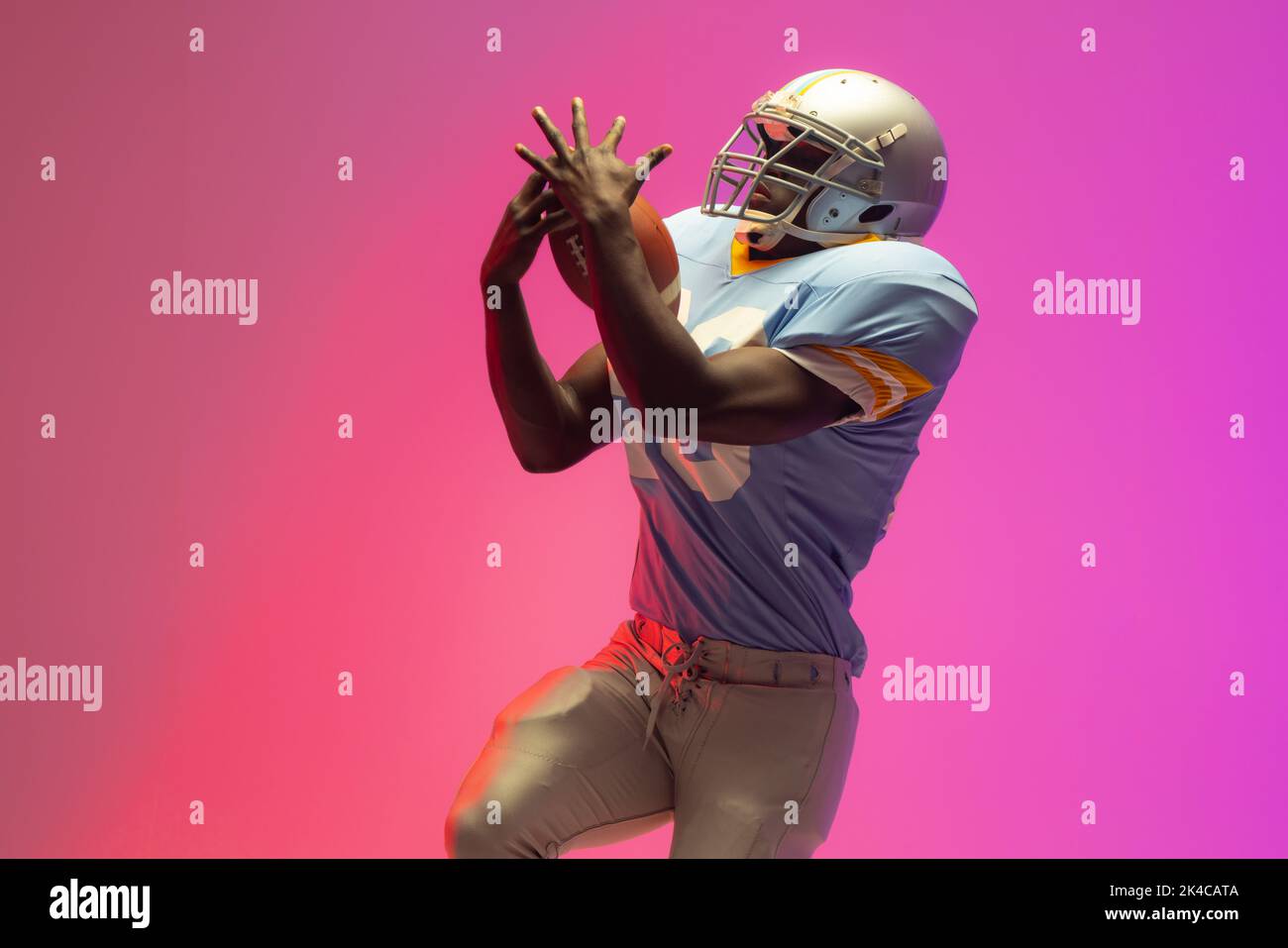 African american male american football player holding ball with neon pink lighting. Sport, movement, training and active lifestyle concept. Stock Photo