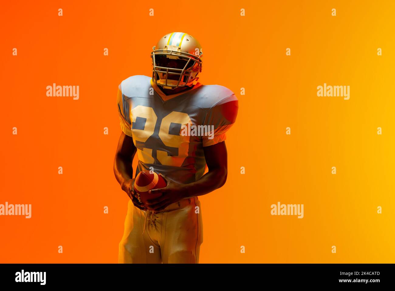 African american male american football player holding ball with neon orange lighting. Sport, movement, training and active lifestyle concept. Stock Photo