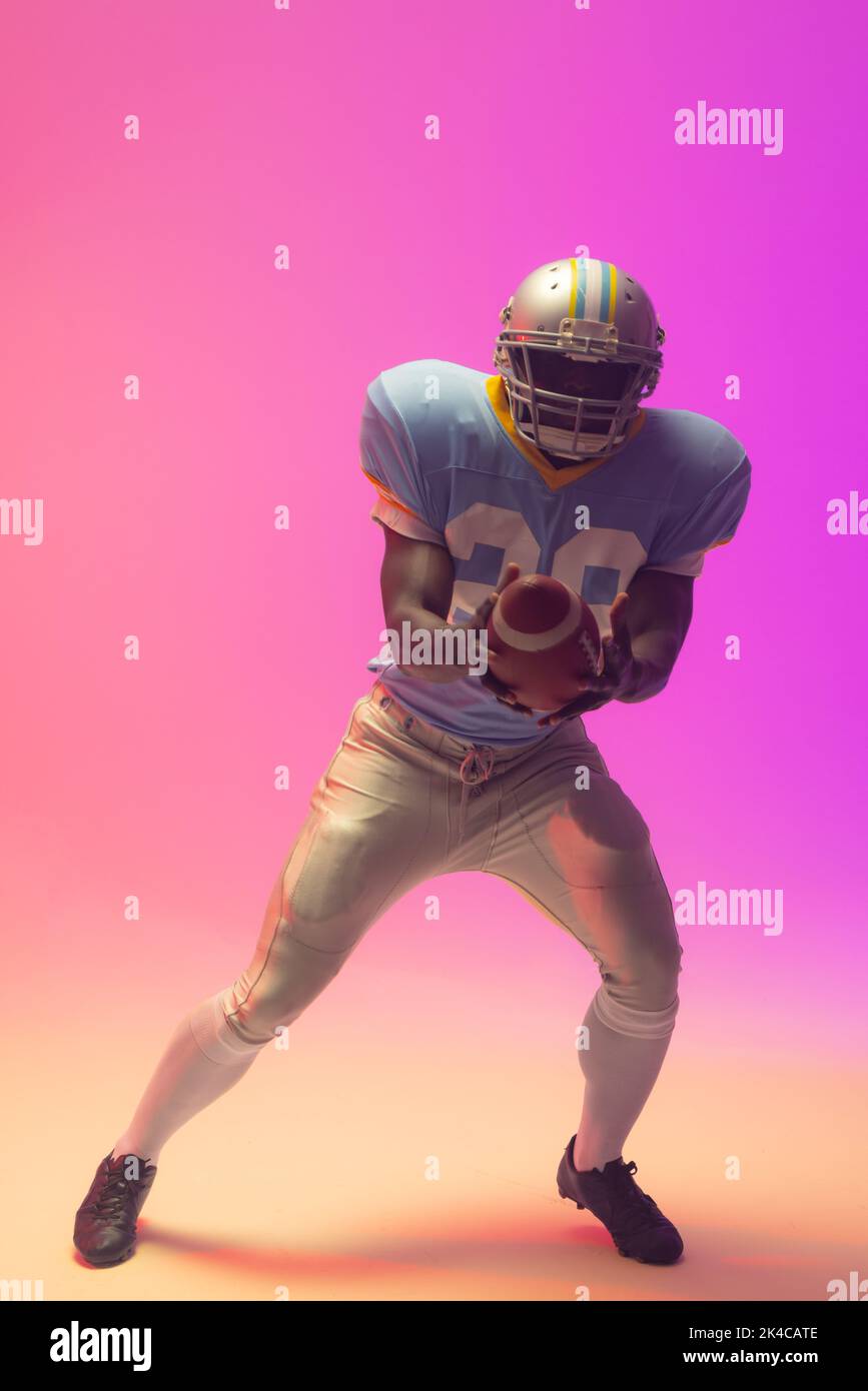 African american male american football player holding ball with neon pink lighting Stock Photo