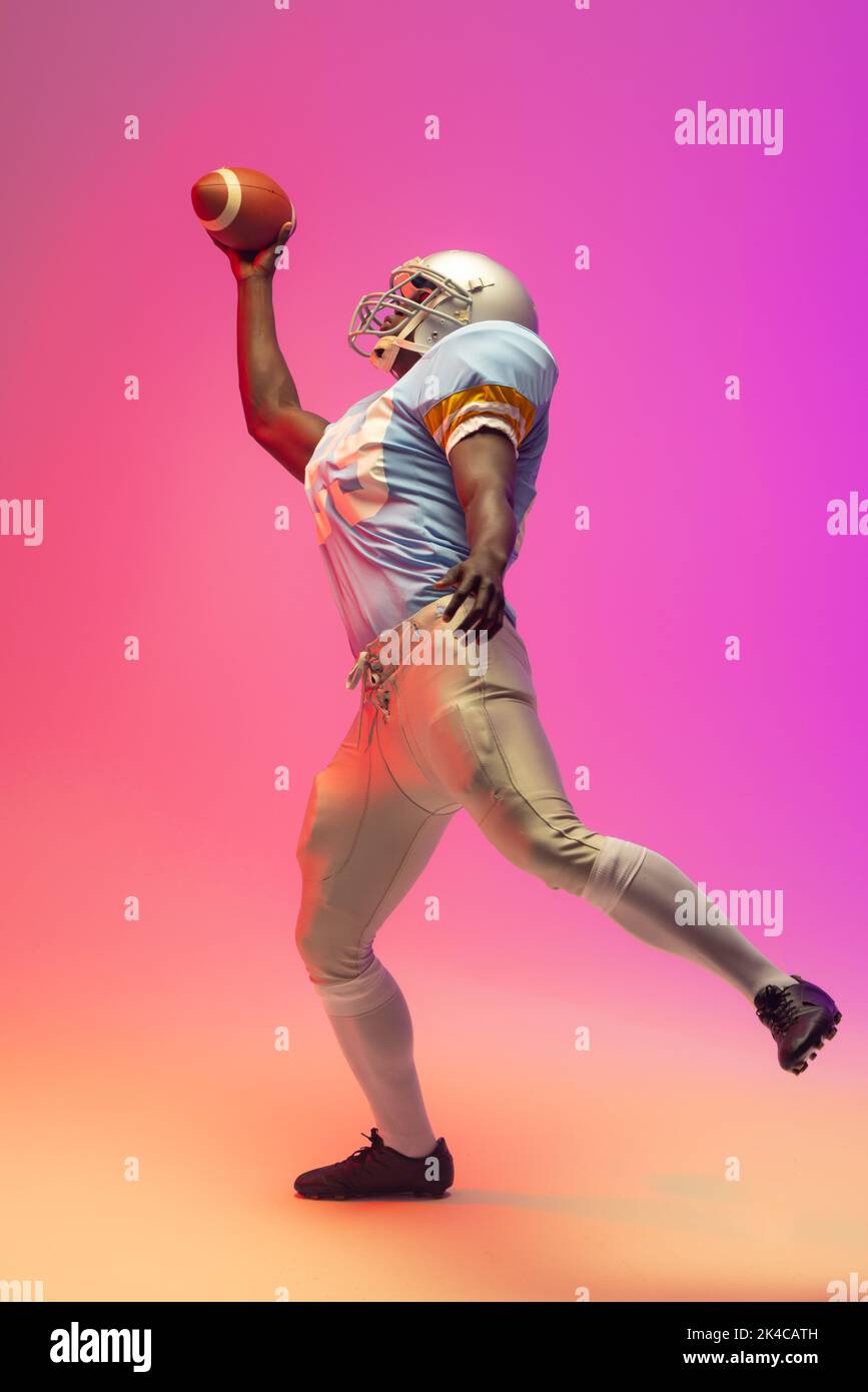 African american male american football player holding ball with neon pink lighting. Sport, movement, training and active lifestyle concept. Stock Photo