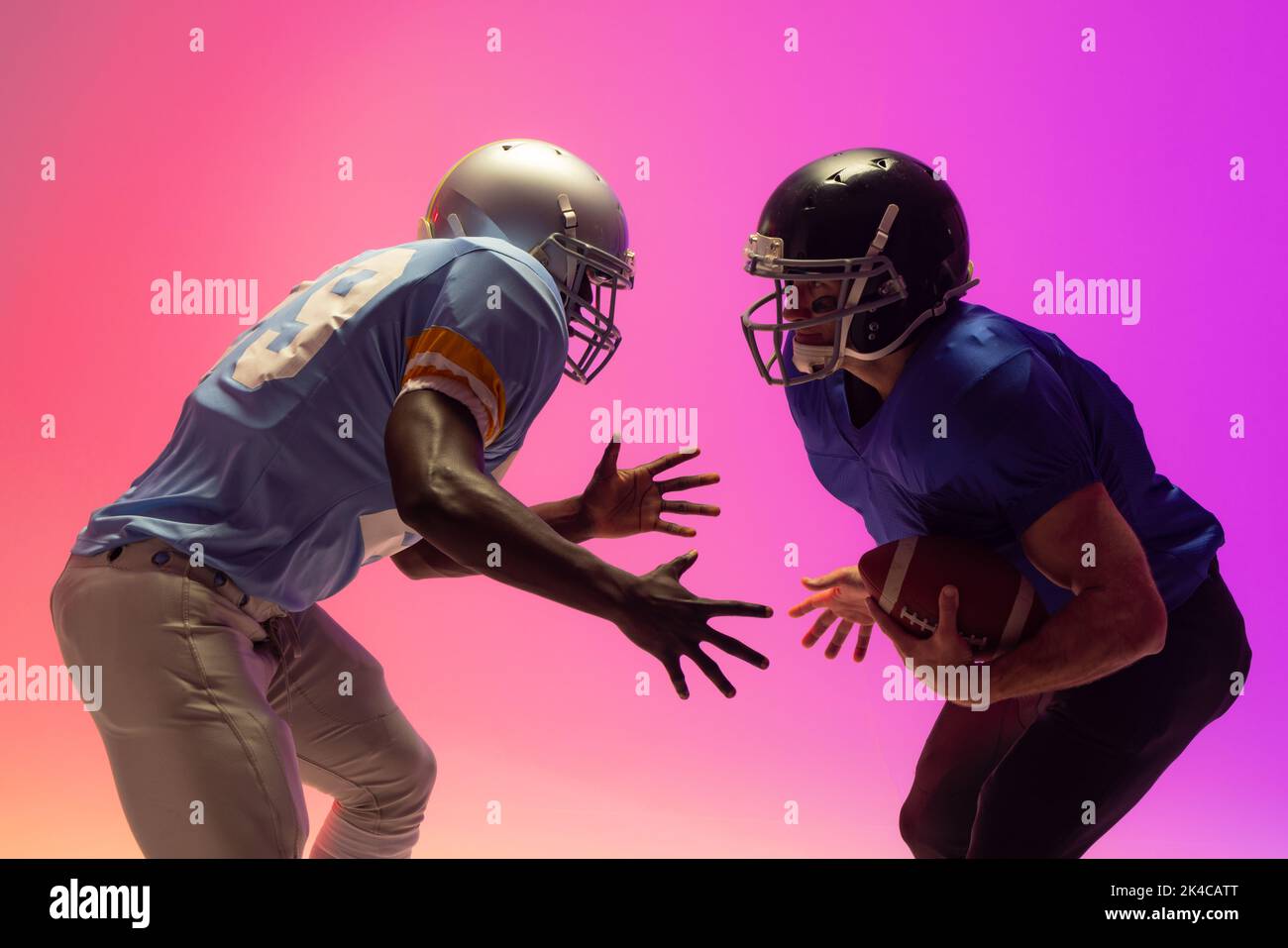 Diverse male american football players holding ball with neon pink lighting. Sport, movement, training and active lifestyle concept. Stock Photo