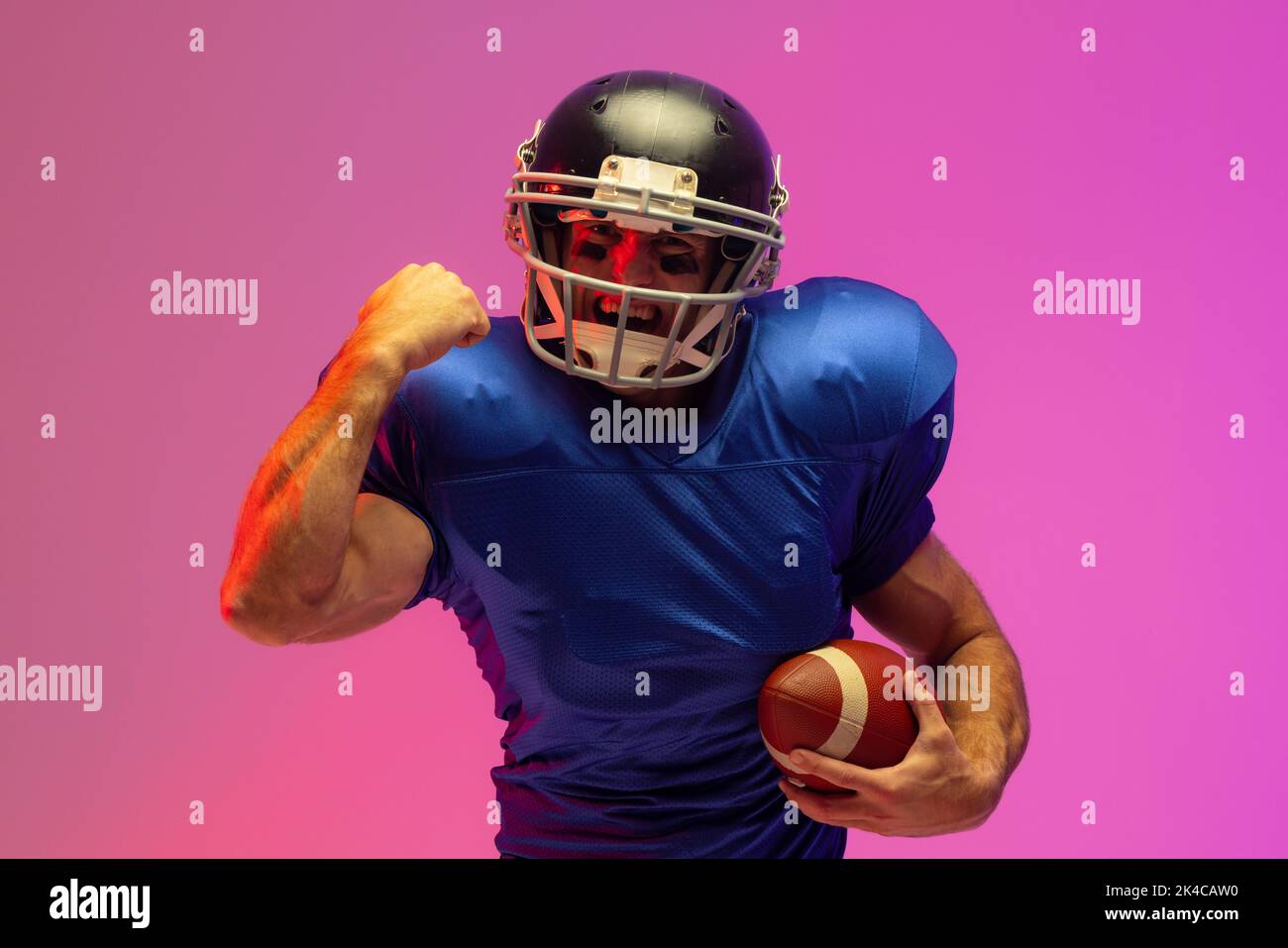 Caucasian male american football player holding ball with neon pink lighting. Sport, movement, training and active lifestyle concept. Stock Photo
