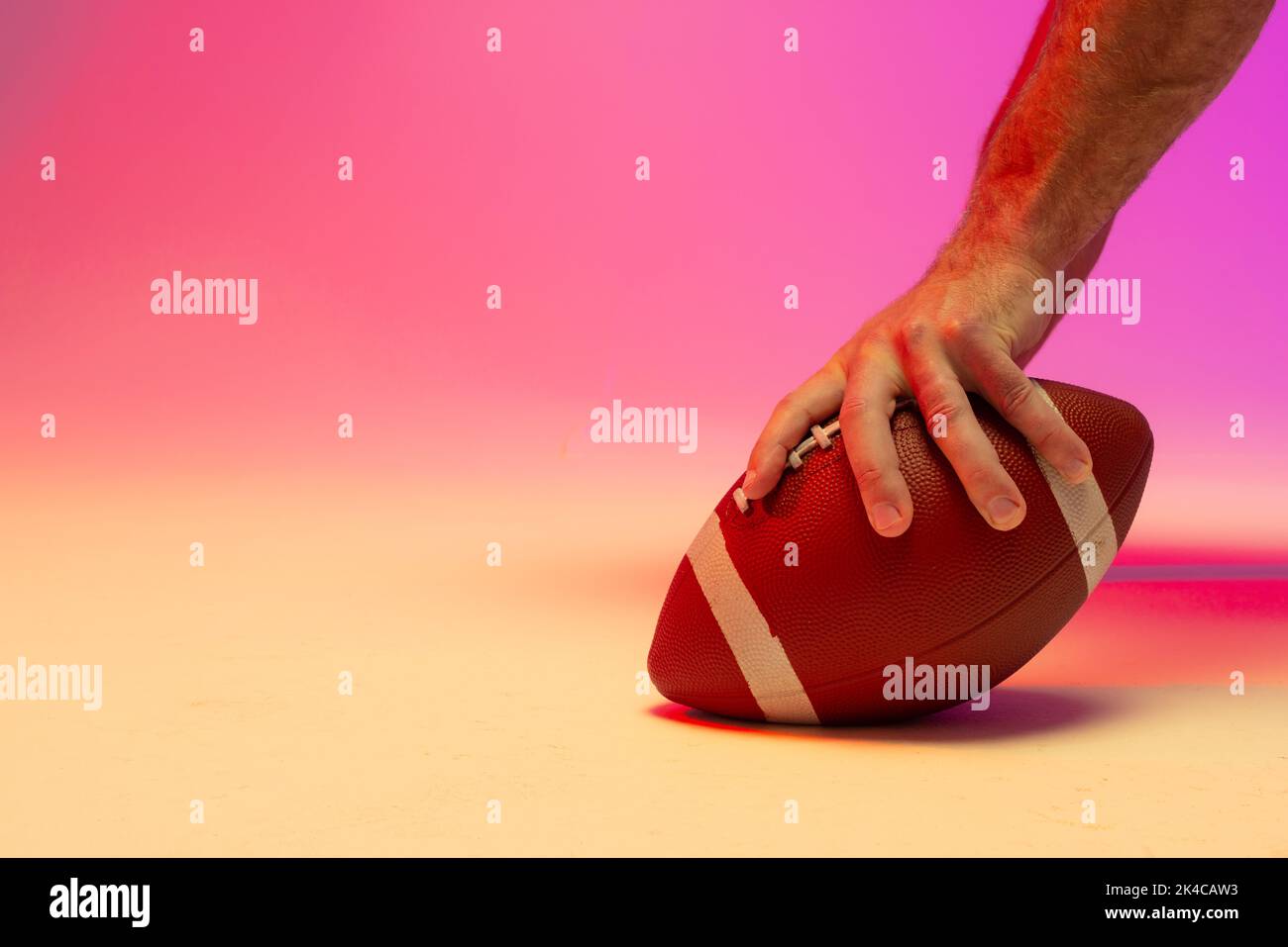 Hand of caucasian male american football player holding ball with neon pink lighting. Sport, movement, training and active lifestyle concept. Stock Photo