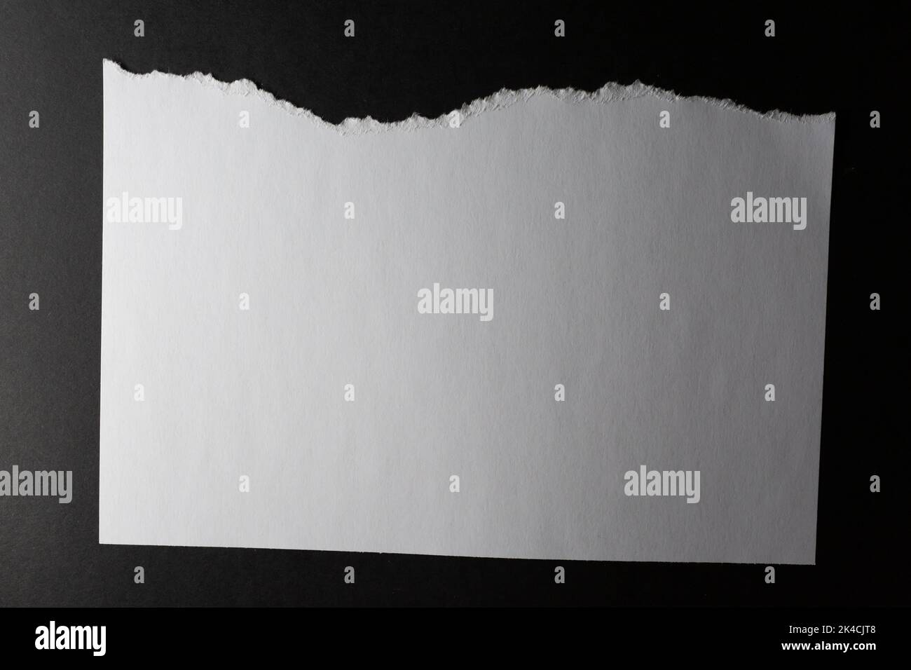 Horizontal sheet of white paper with torn top edge on black background ...