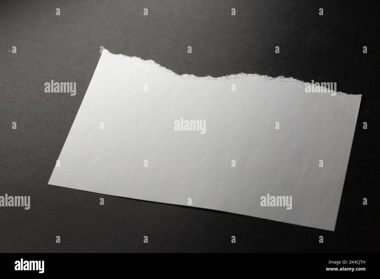 Horizontal sheet of white paper with torn top edge on black background ...