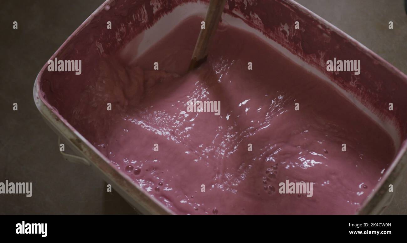 Image of pink paint being stirred in a rectangular white plastic paint