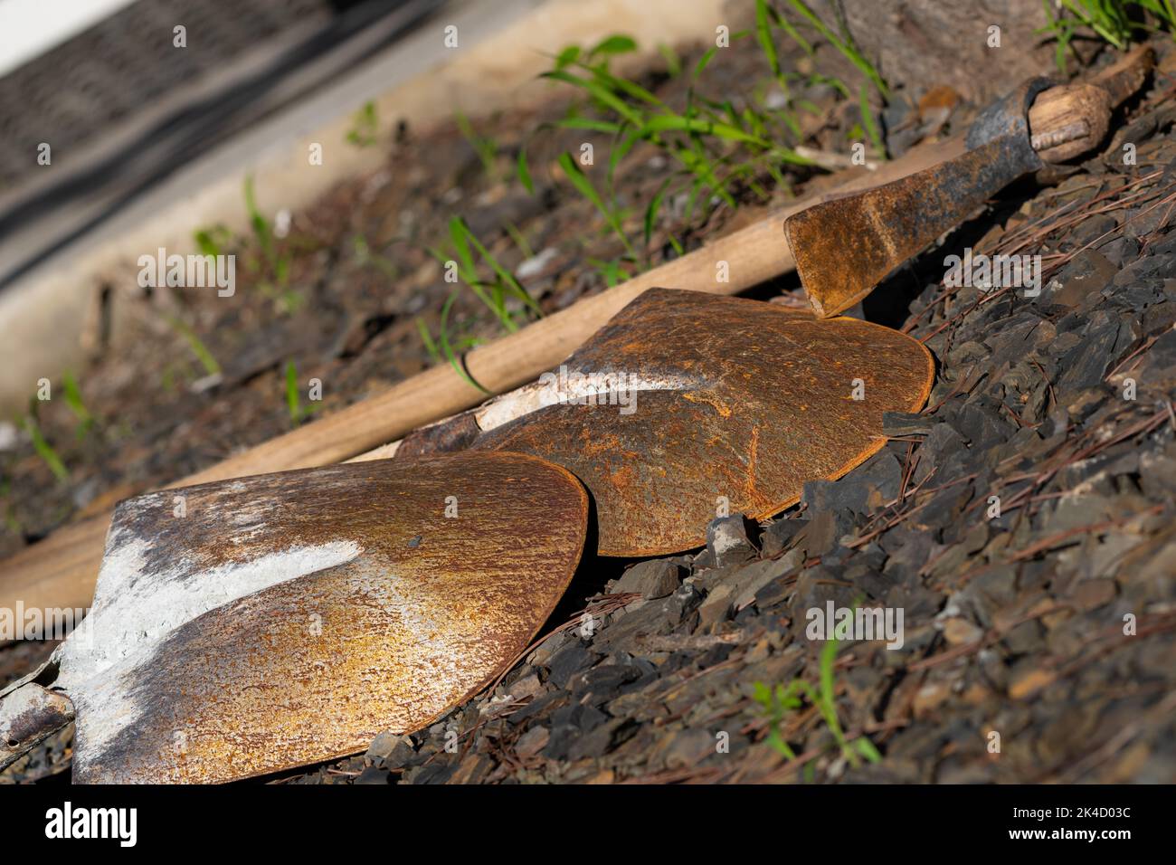 A closeup shot of rusted shovels and a rusted pick axe laid out on the ground Stock Photo