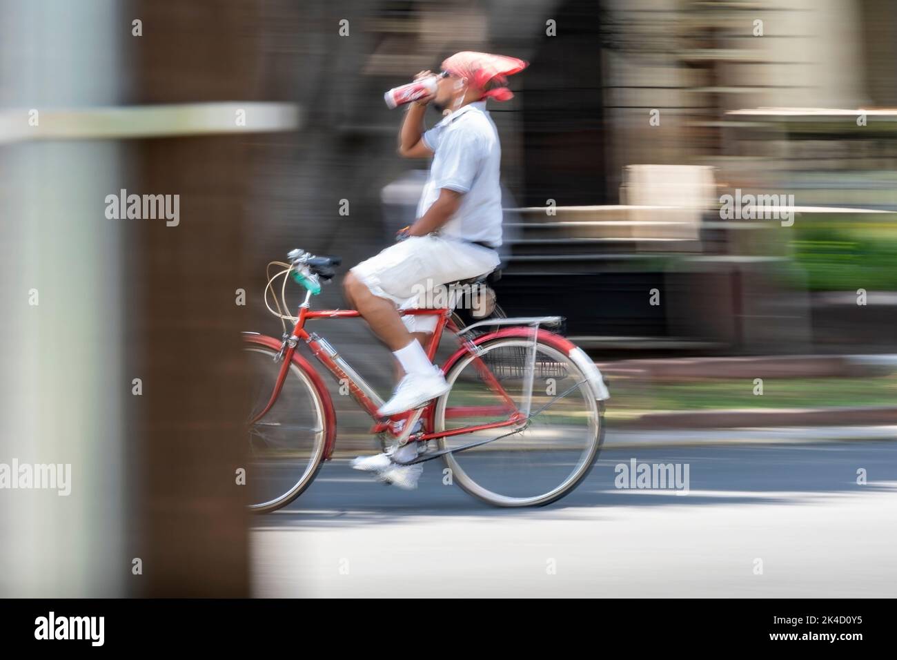 young man on bicycle, drinking beer and paleacate on his head, walking on a sunday, photo with swept background and out of focus Stock Photo