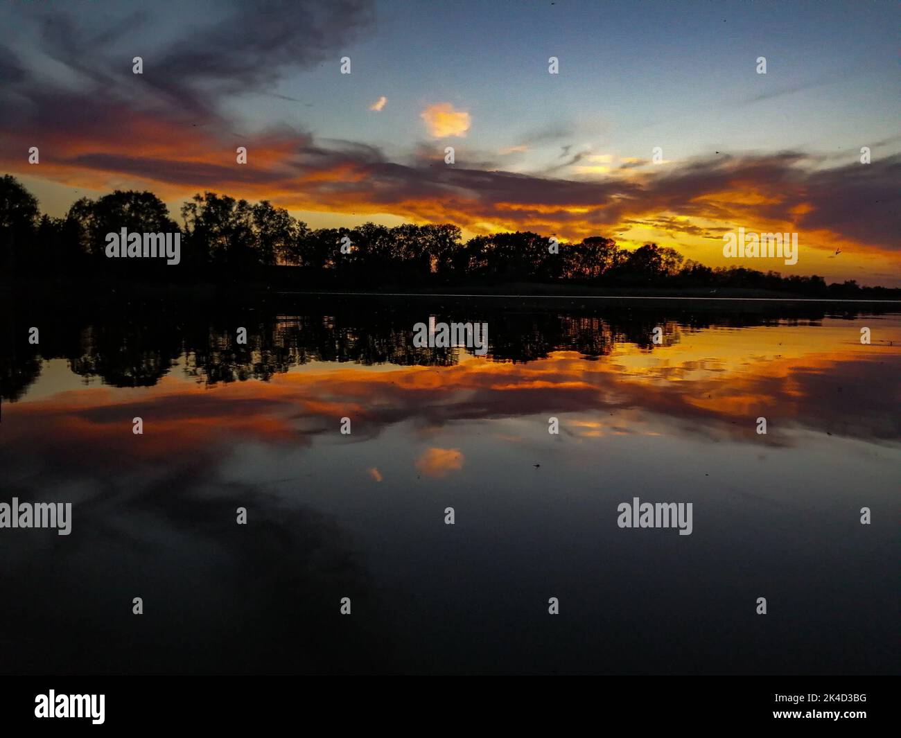 A gorgeous sunset over a reflective lake with silhouettes of trees ...