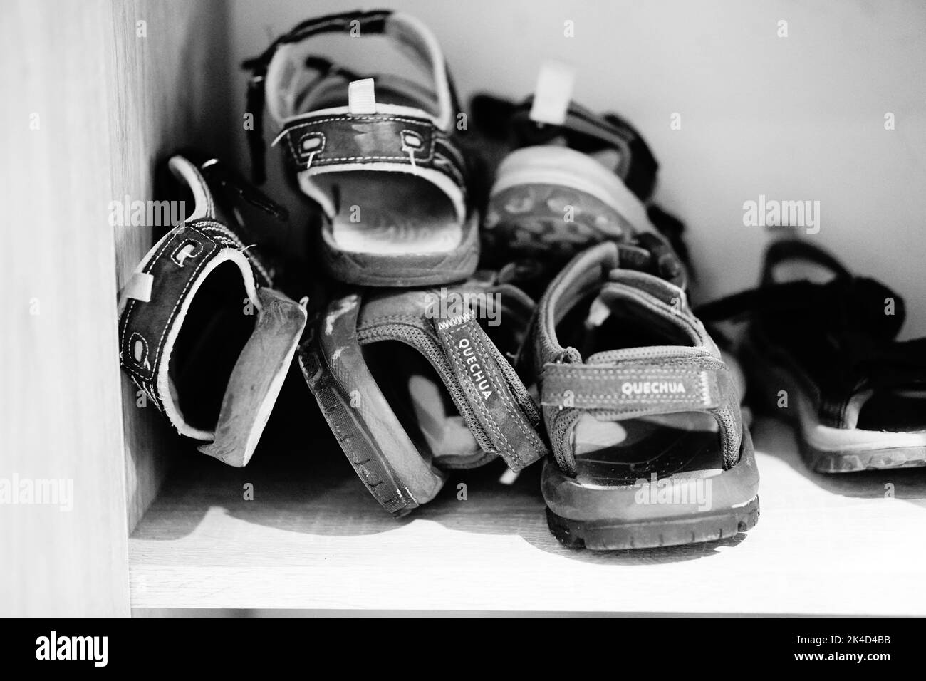 A black and white closeup shot of mix of shoes and sandals on wooden shelf. Stock Photo