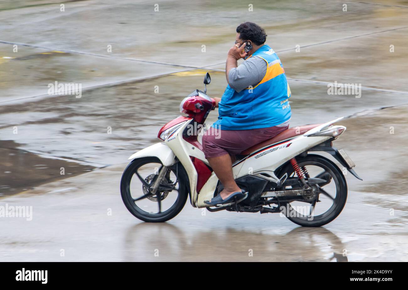 SAMUT PRAKAN, THAILAND, SEP 26 2022, A moto taxi driver calls from mobile phone while driving on wet road Stock Photo