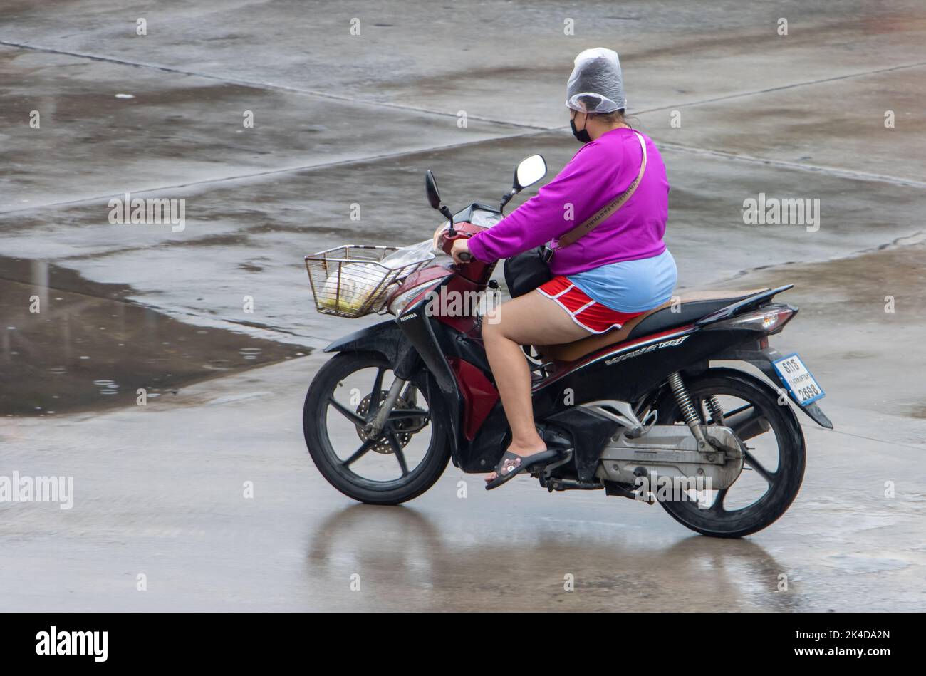 SAMUT PRAKAN, THAILAND, SEP 26 2022, A woman rides a motorcycle with a plastic bag on her head to protect from the rain Stock Photo