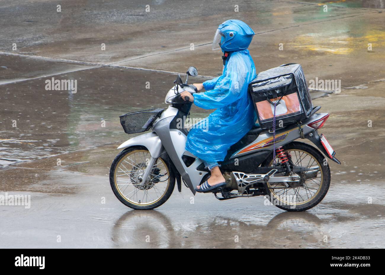A delivery worker rides a motorcycle with a delivery box at rainy weather Stock Photo