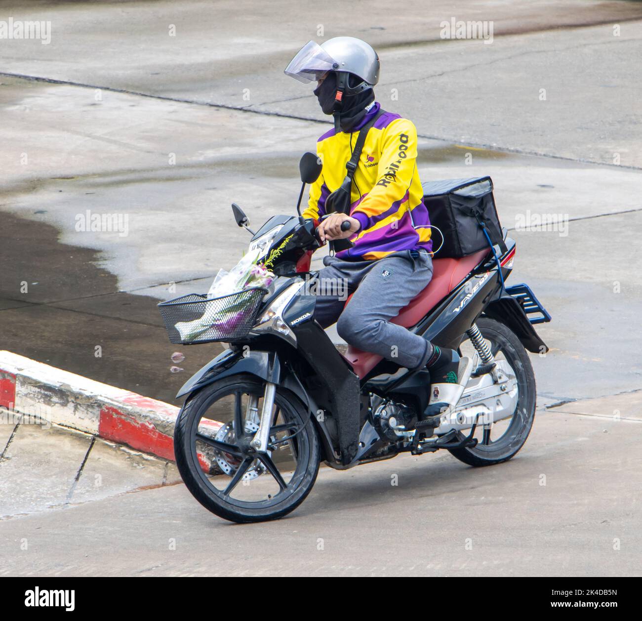 SAMUT PRAKAN, THAILAND, SEP 23 2022, A food delivery worker rides a motorcycle with a delivery box Stock Photo