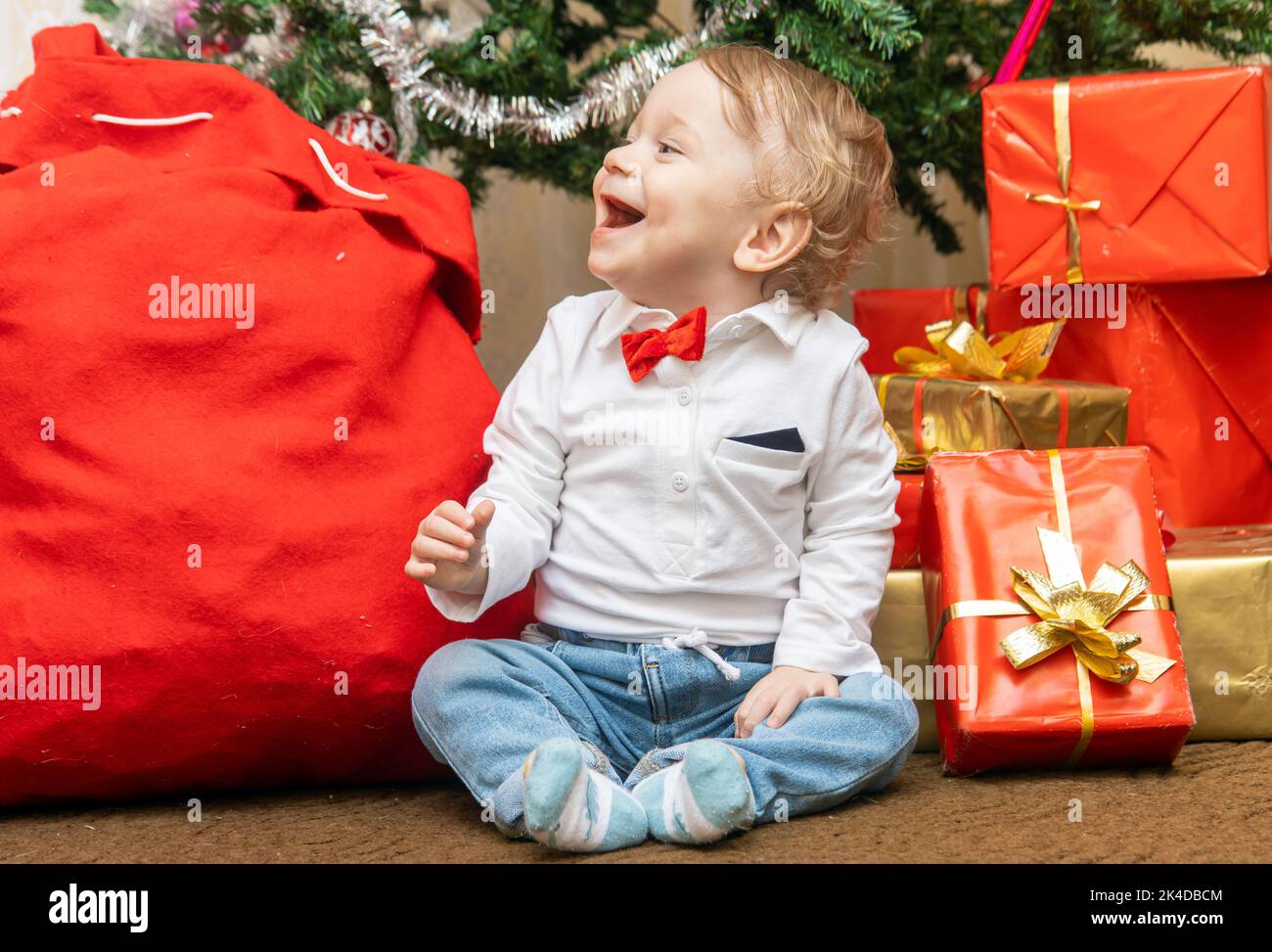 Little boy sits near Christmas presents and laughs Stock Photo