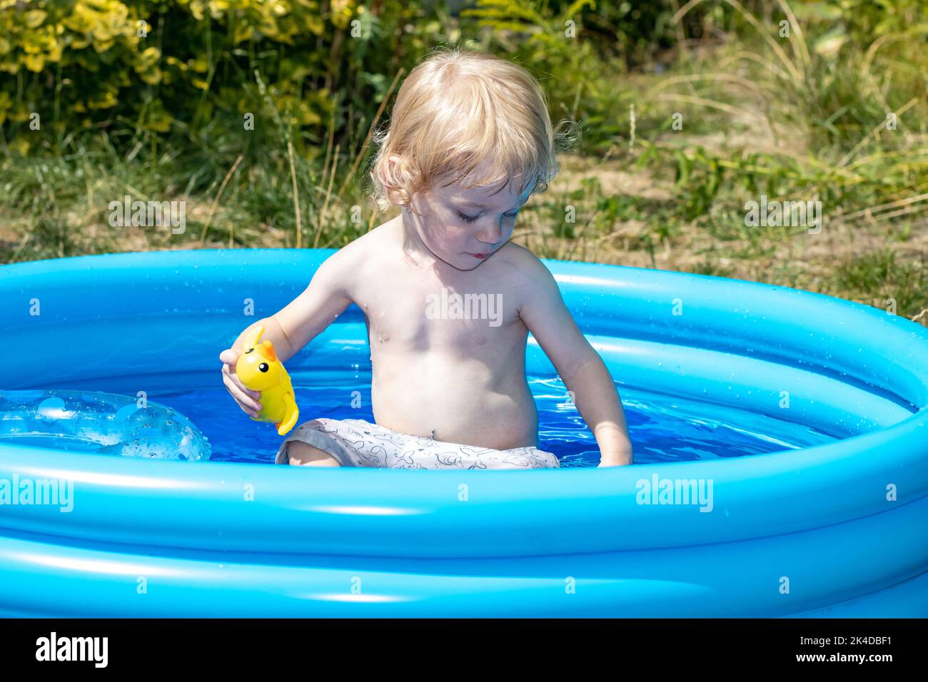 A little boy is playing in the inflatable pool in the summer garden Stock Photo