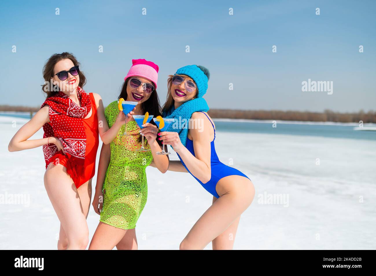 Three female friends in swimsuits drink blue alcoholic cocktails on a