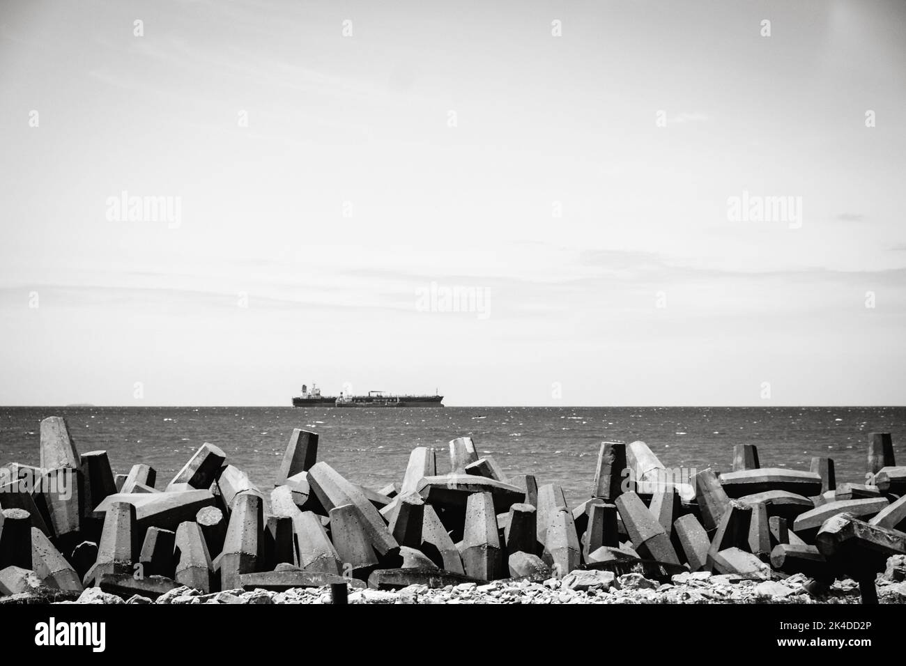 A grayscale of a beach view with garbage cups pile and a flowing ship