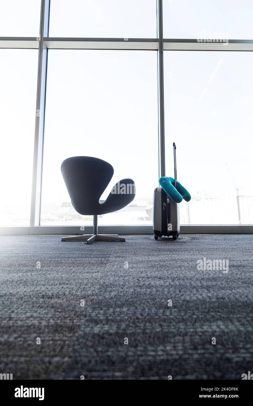 An empty chair and a carry on in front of a giant airport window