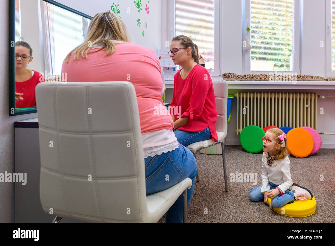 Mother and young daughter in therapist office during counselling assesment meeting. Living with disabilty and community support system. Stock Photo