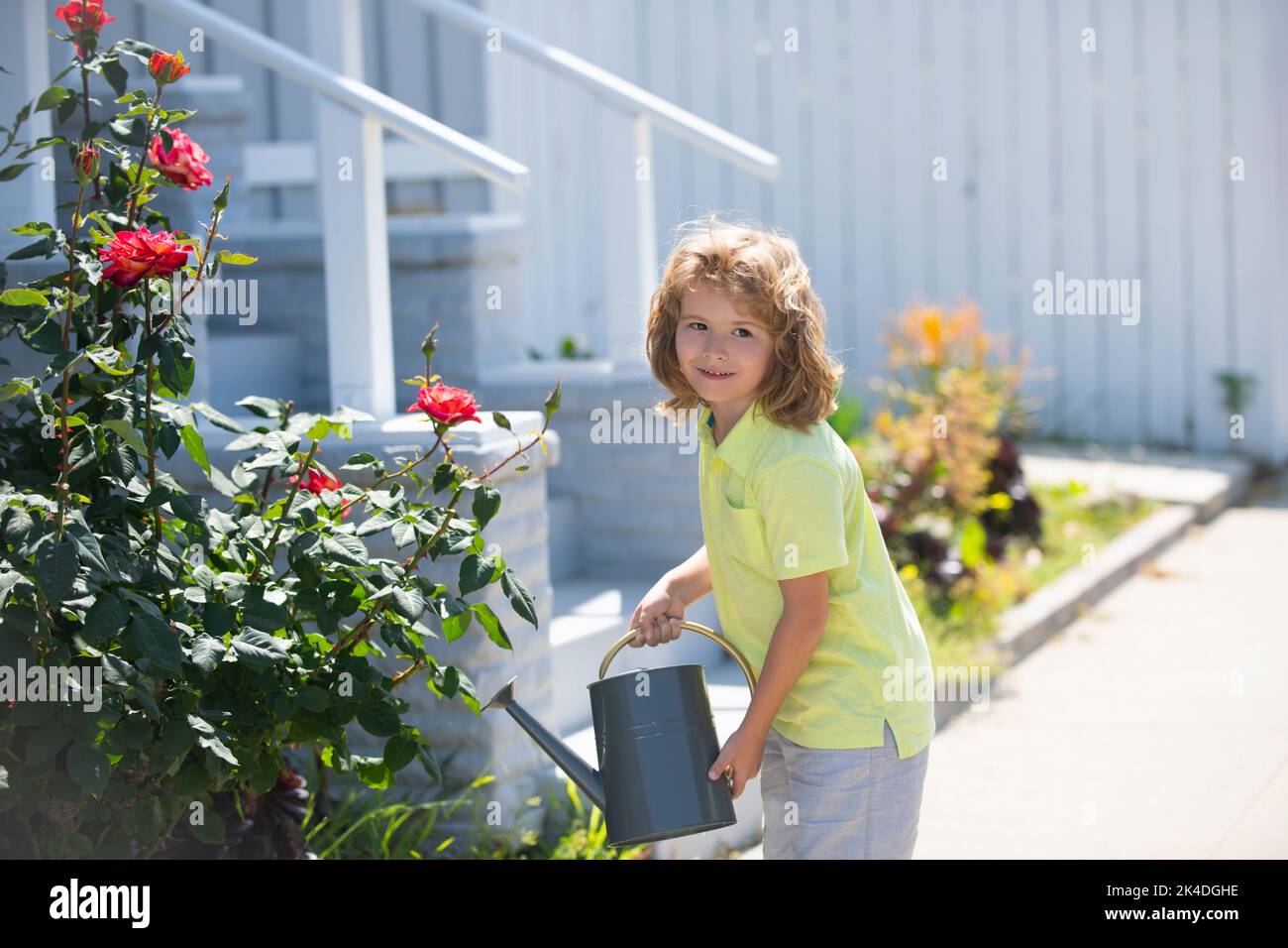 Cute little toddler boy watering plants with watering can in the garden