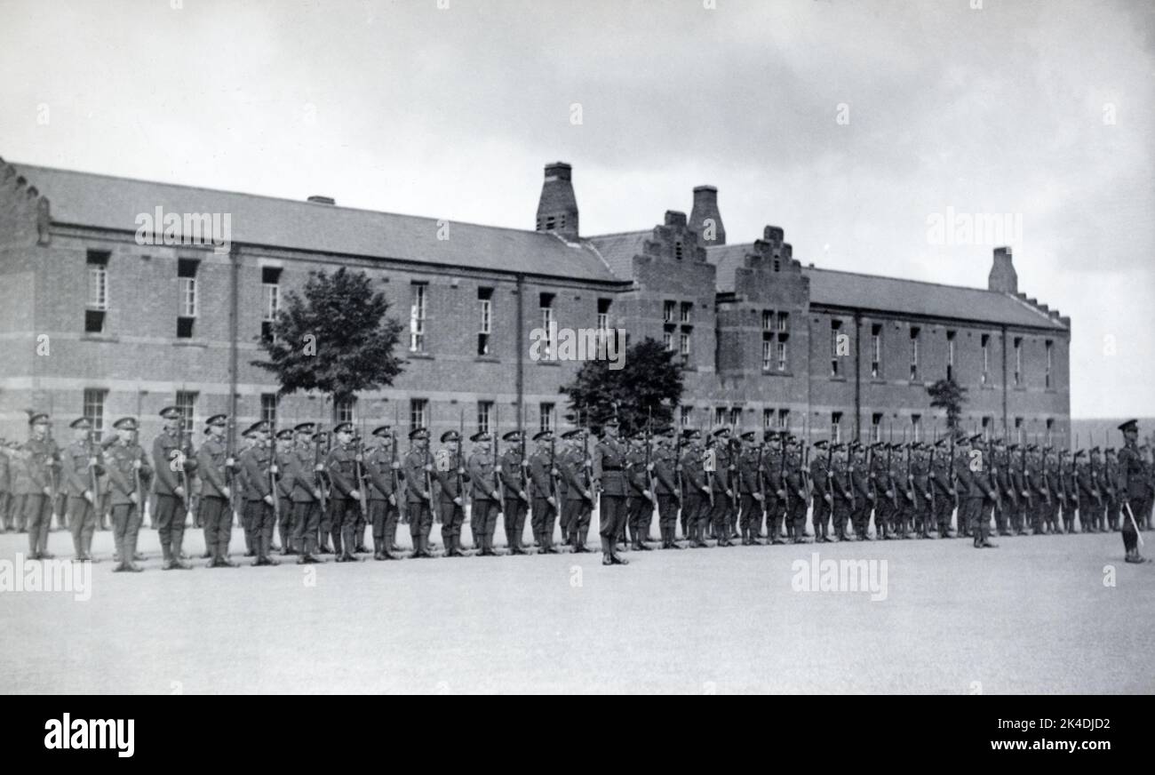 An interwar era picture of British army officers and solidiers on parade presenting arms for a general salute with riles, outside a brick barracks. Stock Photo