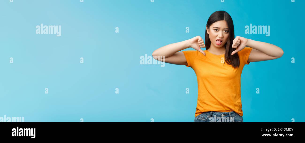 Disappointed upset and unimpressed cute childish asian girl dark haircut, frowning cringing dislike, aversion, show thumbs-down stick tongue disgust Stock Photo