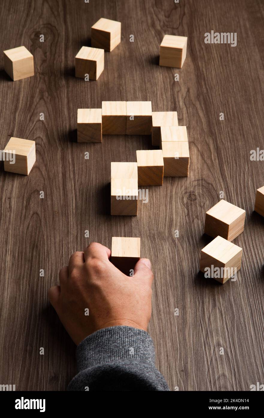 Hand solving a problem, arranging wooden blocks into a question mark on a wooden table Stock Photo