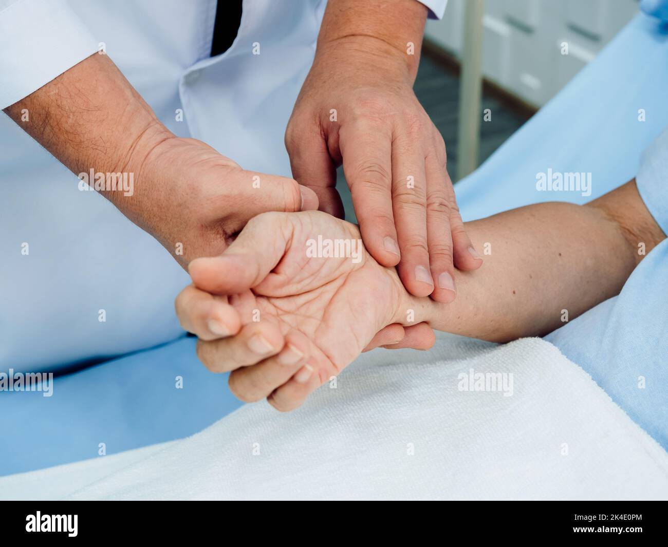 Close up doctor's hand in white lab coat holding elderly patient's hand who lying on the bed for checking examining heartbeat pulse by fingers in reco Stock Photo