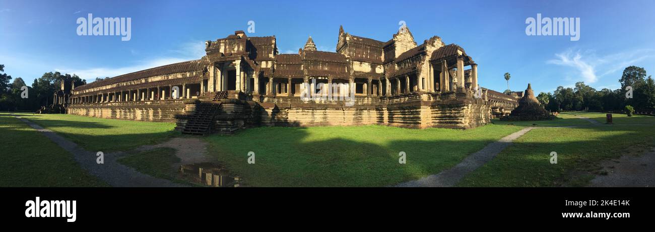 A panoramic shot of Angkor Wat temple with precinct, blue sky background, and grass around Stock Photo