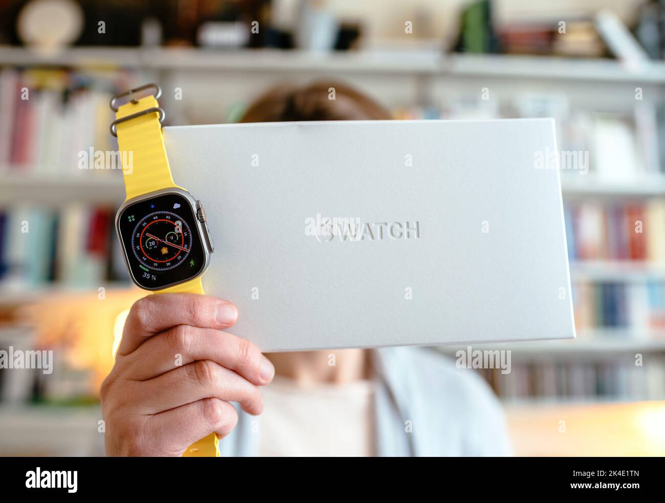 London, United Kingdom - Sept 28, 2022: Woman holding new Apple Computers Apple Watch Ultra next to its innovative packaging - living room bookshelves in background Stock Photo
