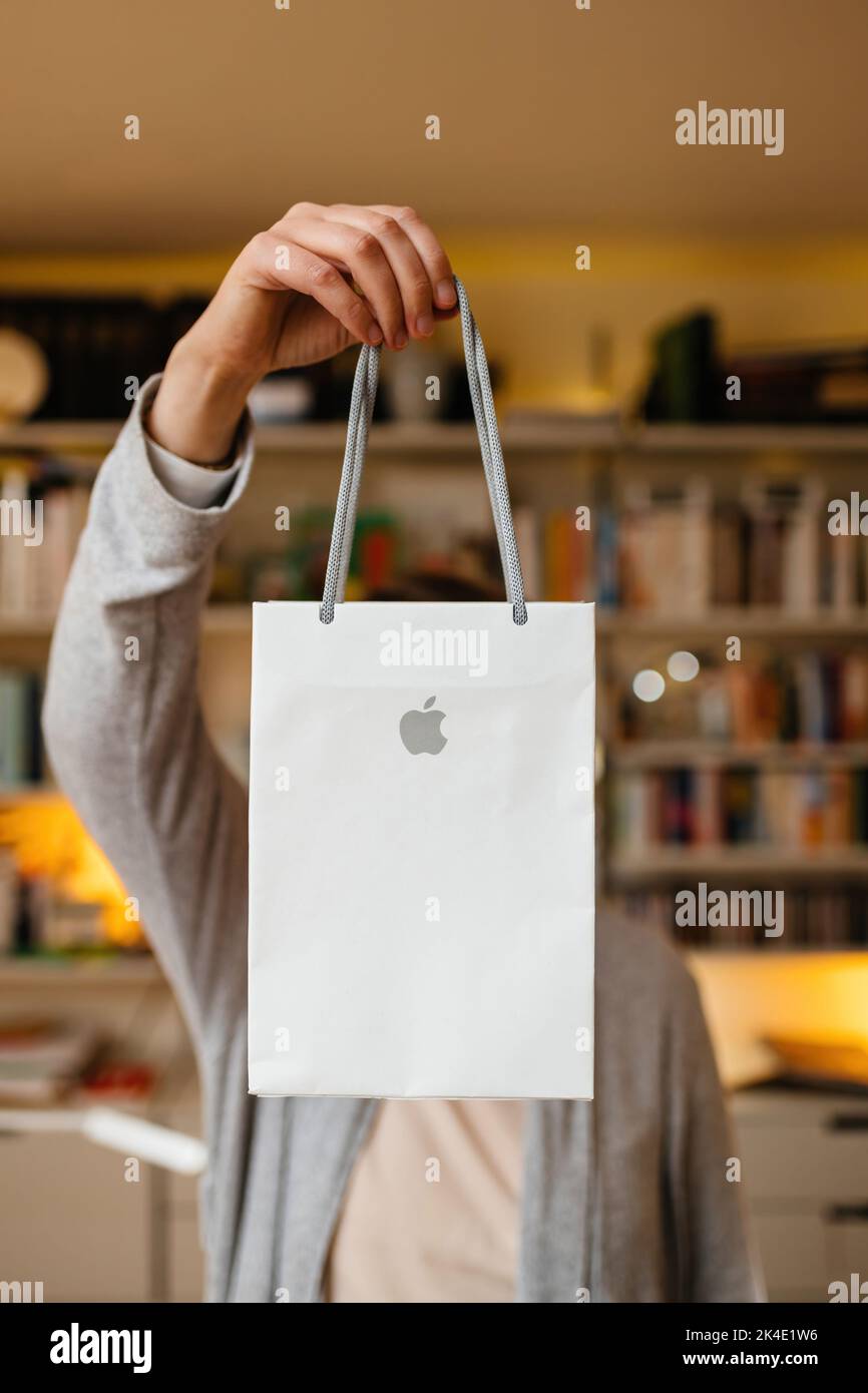 London, United Kingdom - Sept 28, 2022: Woman holding Apple Computers gift paper shopping bag in front of her with living room shelves in background Stock Photo