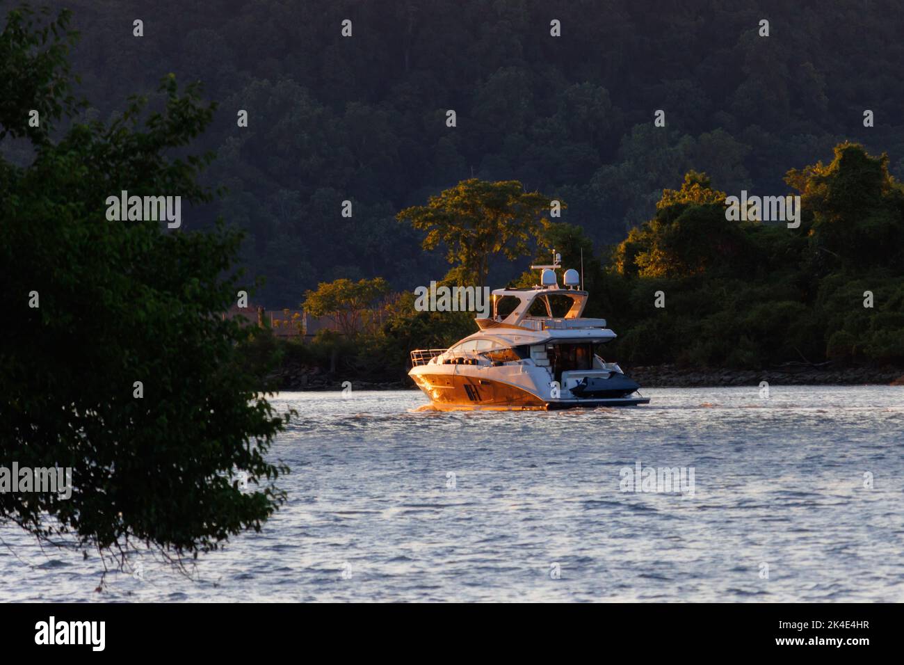 leisure yacht turning a bend on the rippling waters of the Hudson River at the golden hour with summer foliage in the background and foreground, with Stock Photo