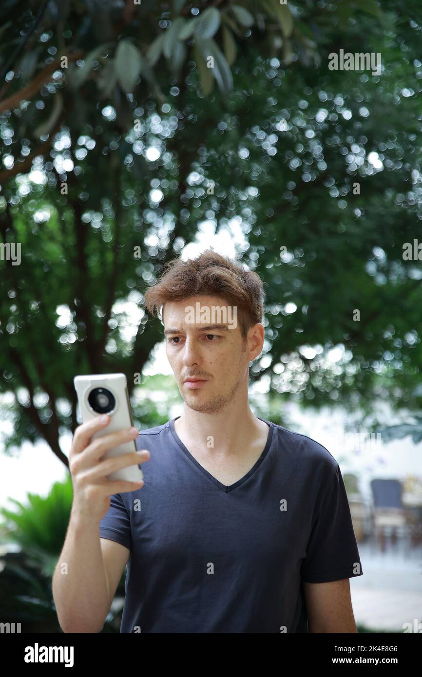 Red haired european man with freckles looking at playing with his mobile phone Stock Photo