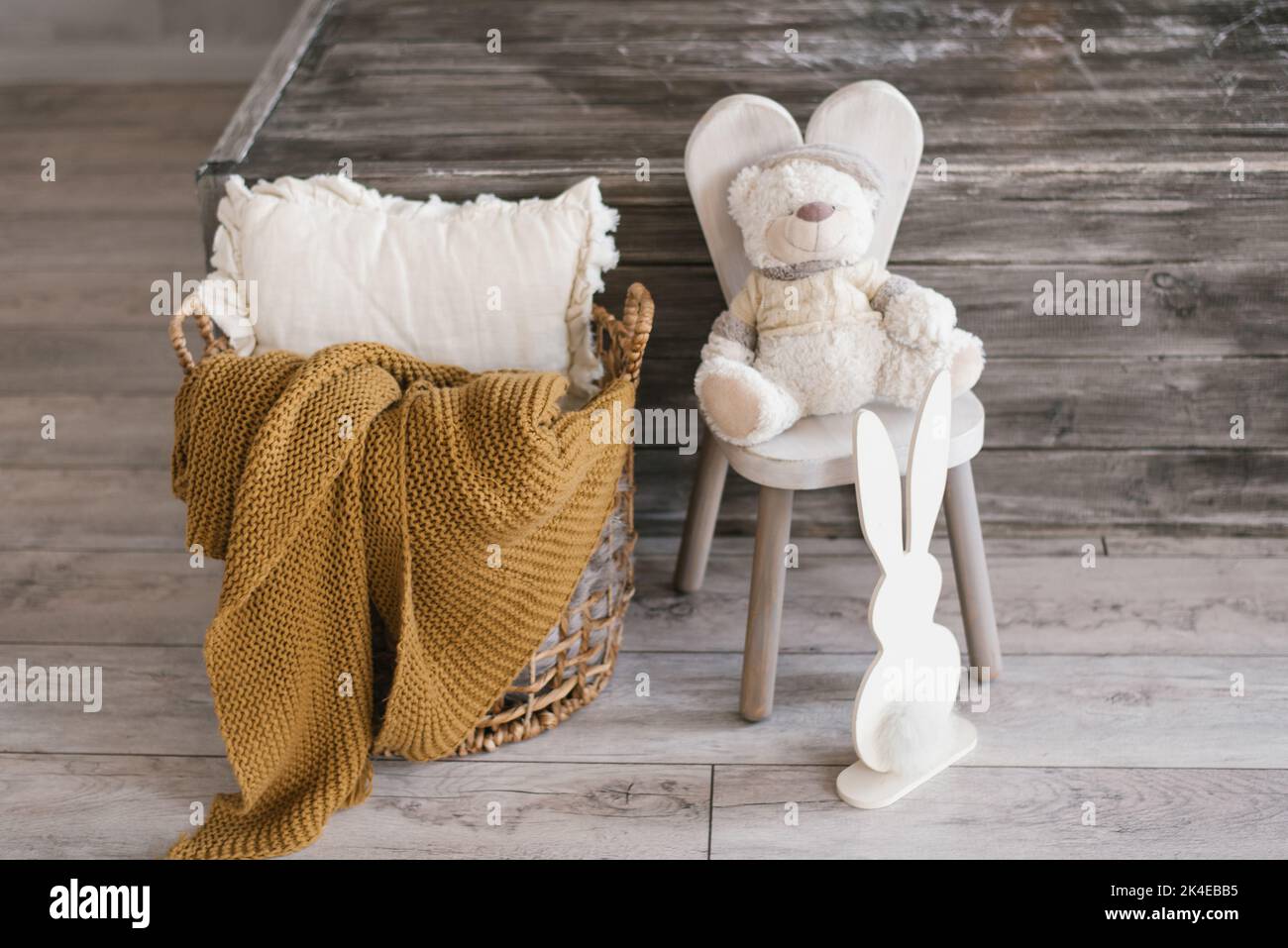 Children's soft toy bear sits on a chair, next to it there is a plywood bunny and a basket with a blanket and a pillow. Accessories in the summer room Stock Photo