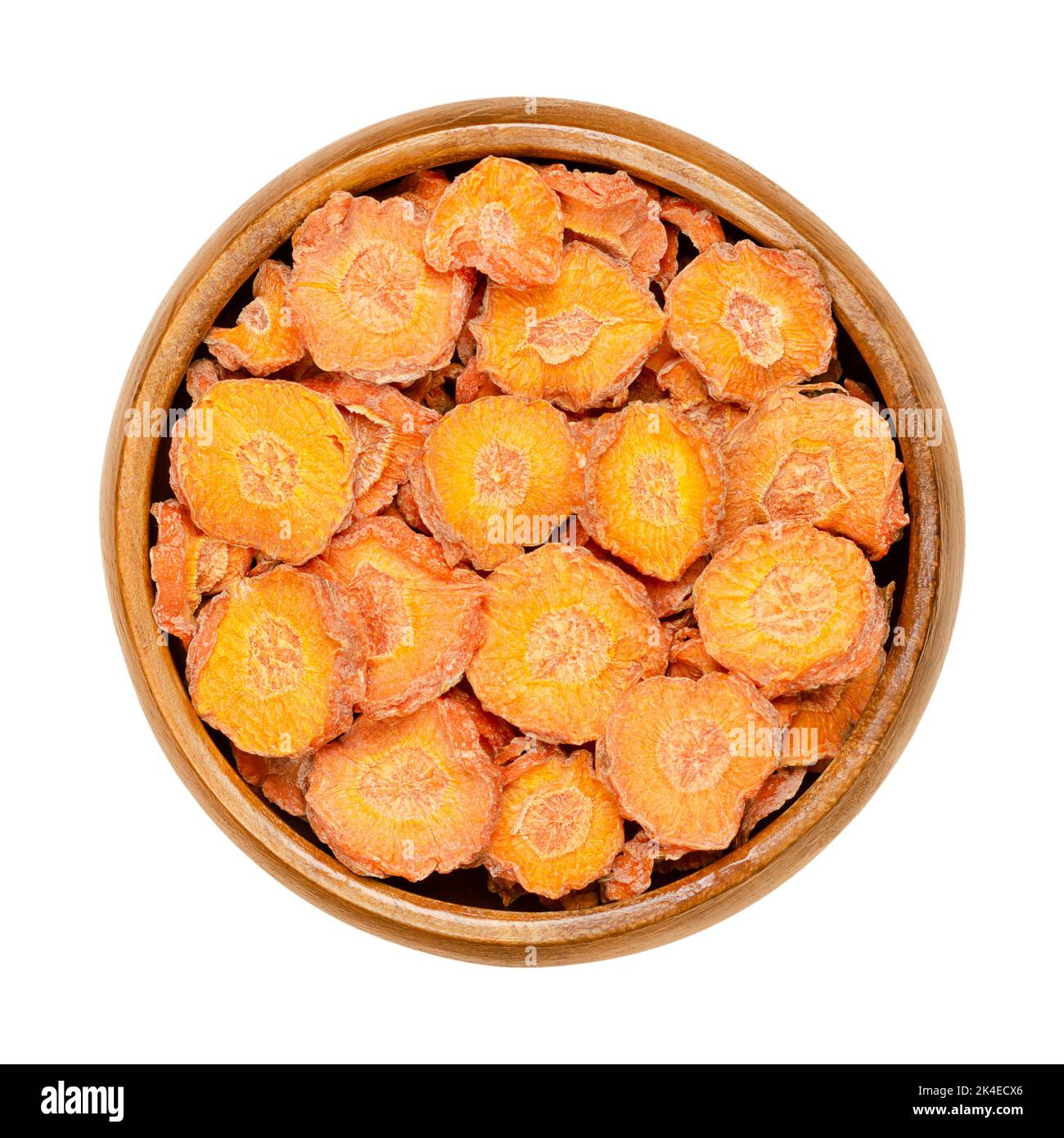 Dehydrated carrot slices in a wooden bowl. Dry disks of Daucus carota, a root vegetable with orange color. Edible taproot pieces. Close up, from above. Stock Photo