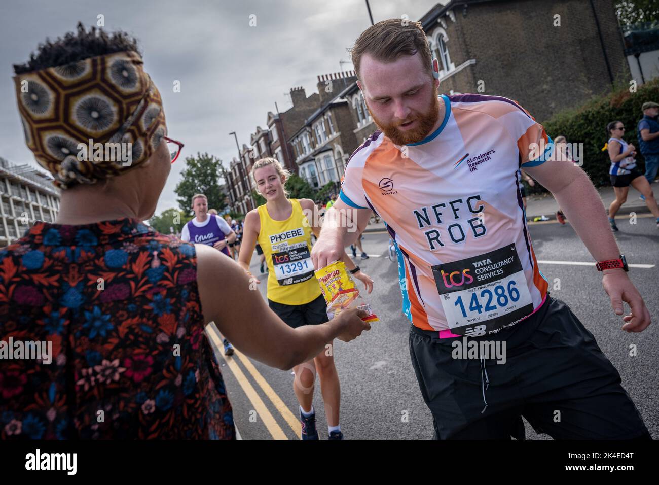 London, UK. 2nd October, 2022. Sweets are handed out by locals as London Marathon passes down Deptford’s Evelyn Street in South East London, the 8 mile mark of the 26.2 mile course where runners are greeted and cheered on by local residents. Credit: Guy Corbishley/Alamy Live News Stock Photo