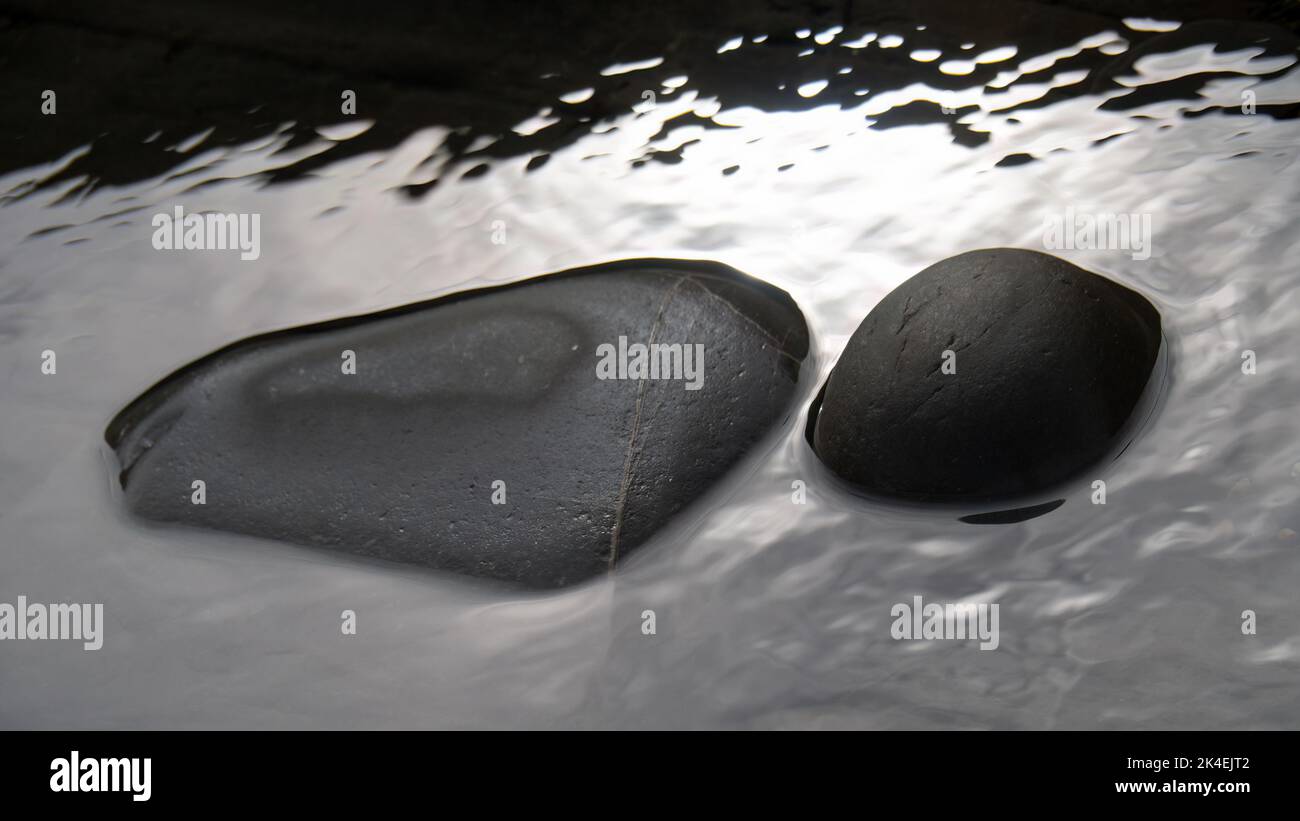 Dark grey rocks in a pool on a beach. Abstract nature background. Stock Photo
