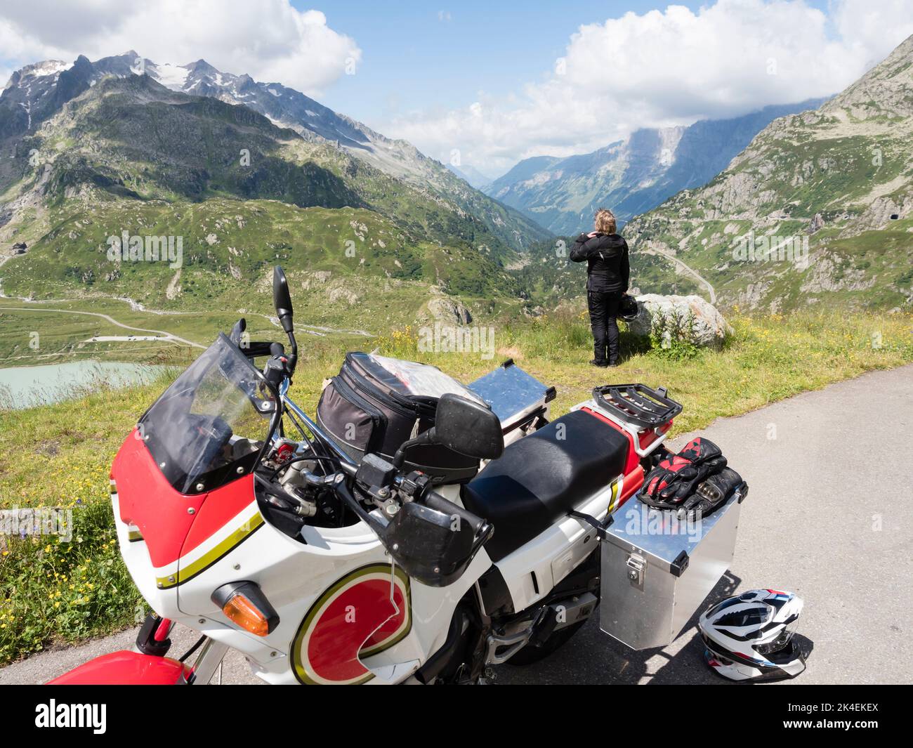 An adventure motorcycle rider is taking a break at a mountain pass in the Swiss alps. Stock Photo