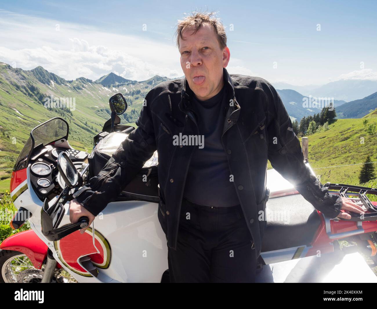 An adventure motorcycle rider during a break with his motorbike at a mountain pass in the Swiss alps. Stock Photo