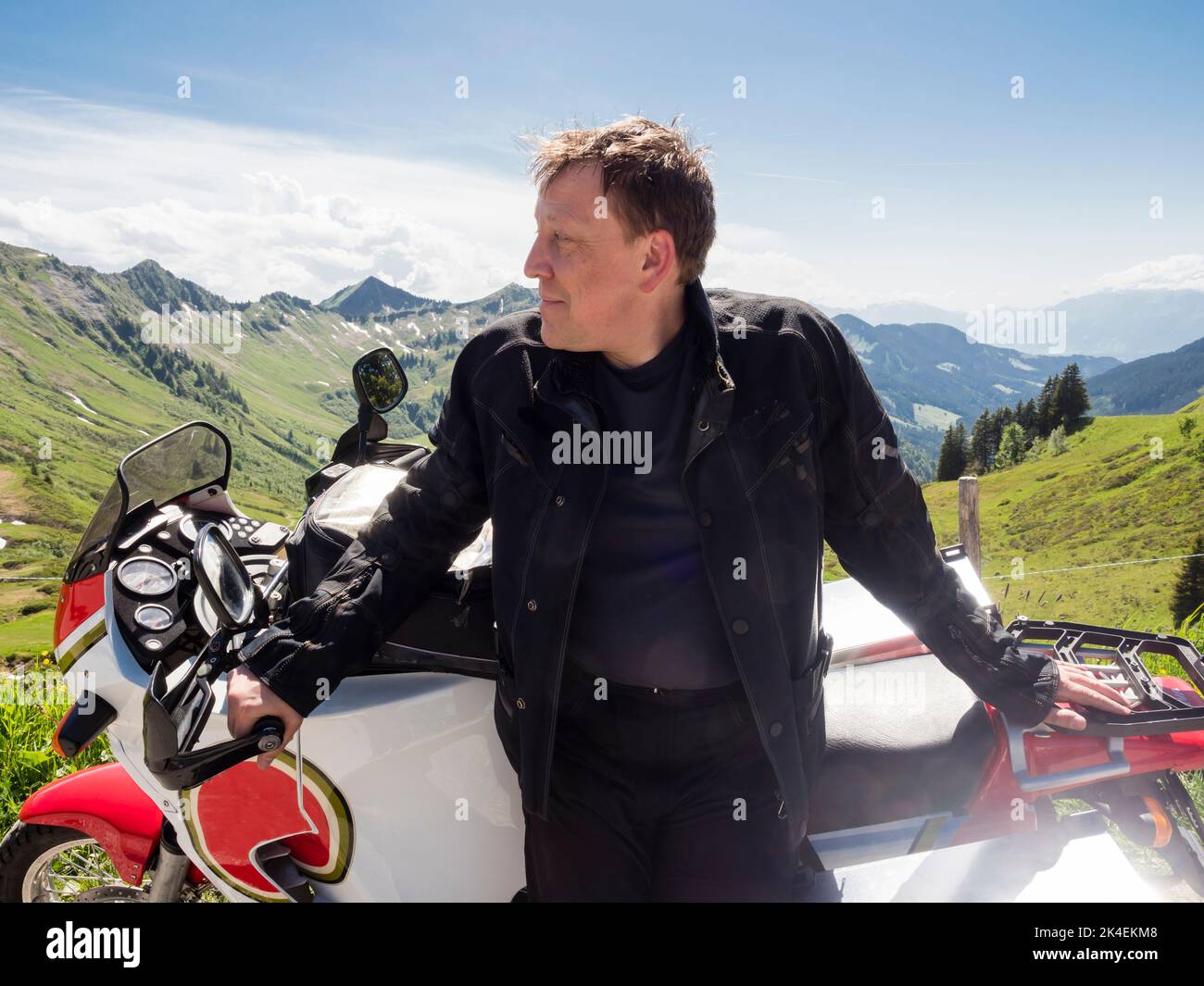 An adventure motorcycle rider during a break with his motorbike at a mountain pass in the Swiss alps. Stock Photo