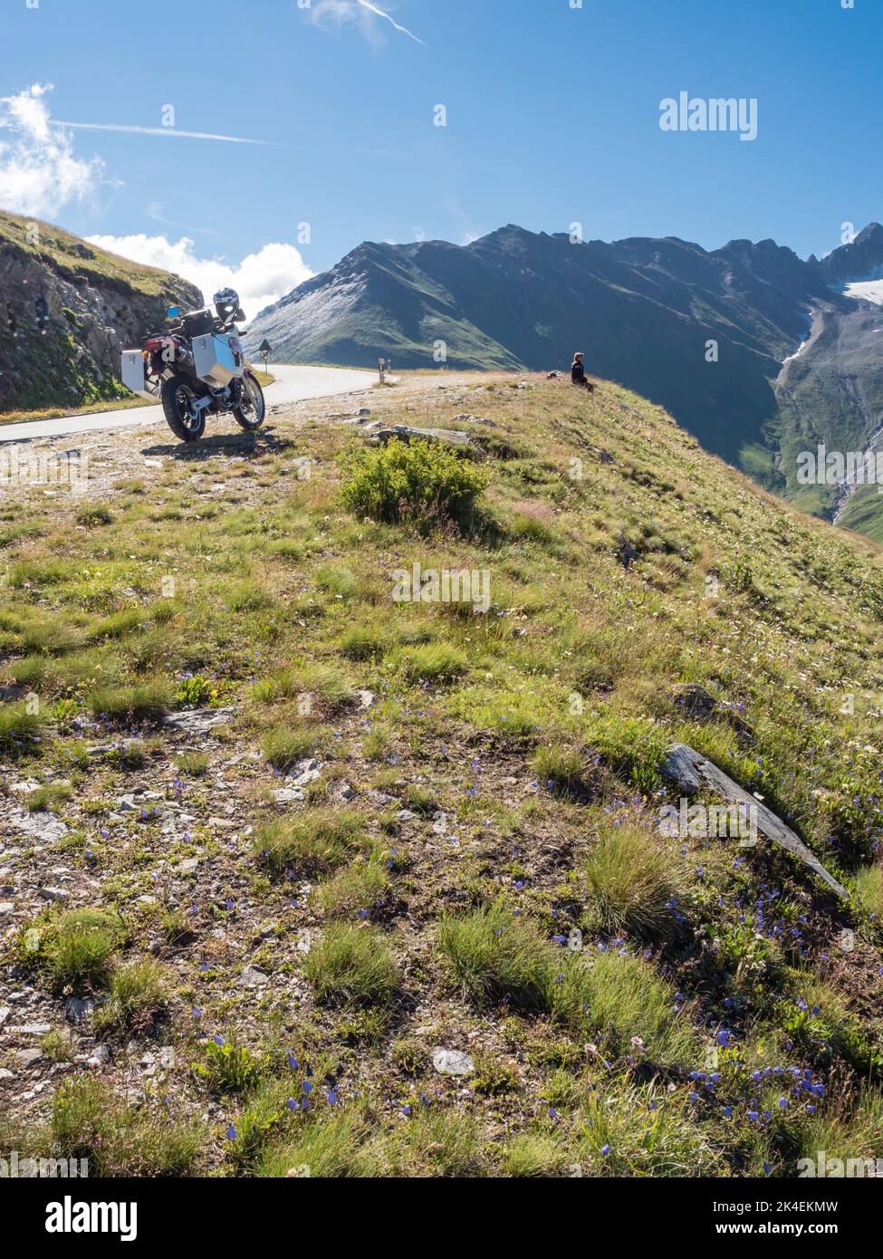 An adventure motorcycle with big aluminum cases is parked at a mountain pass in the European alps. Rear view, low angle view Stock Photo
