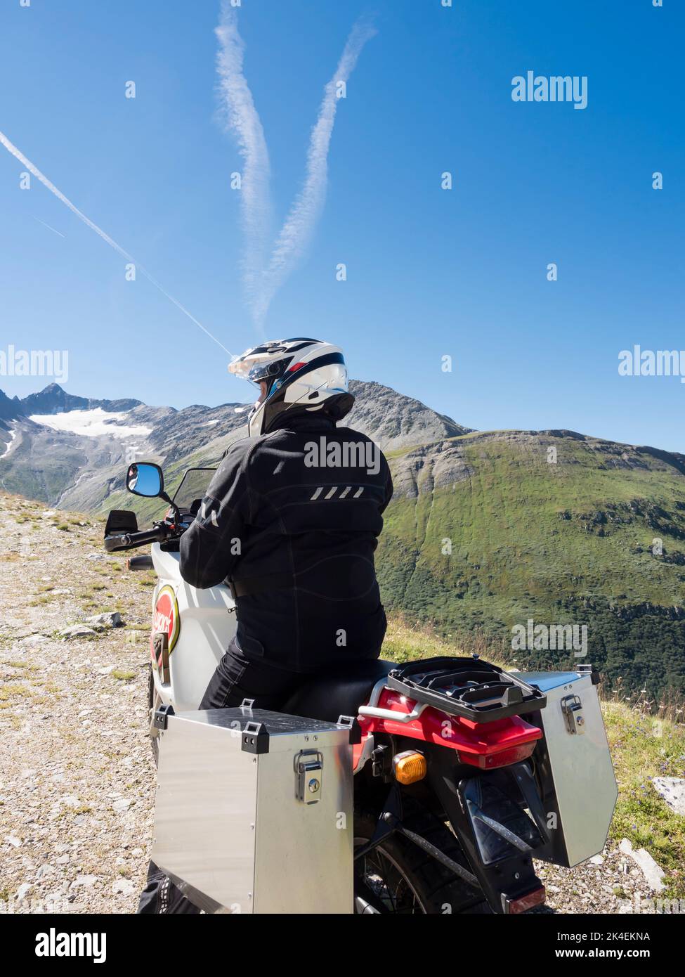 An adventure motorcycle rider at a mountain pass in the Swiss alps. Stock Photo