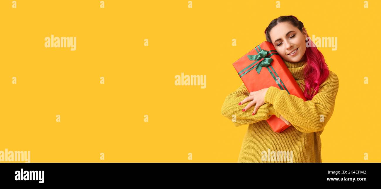 Beautiful woman holding Christmas gift box on yellow background with ...